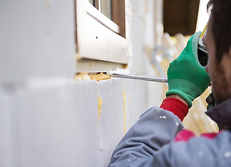 Man applying foam sealant with caulking gun to insulate the window